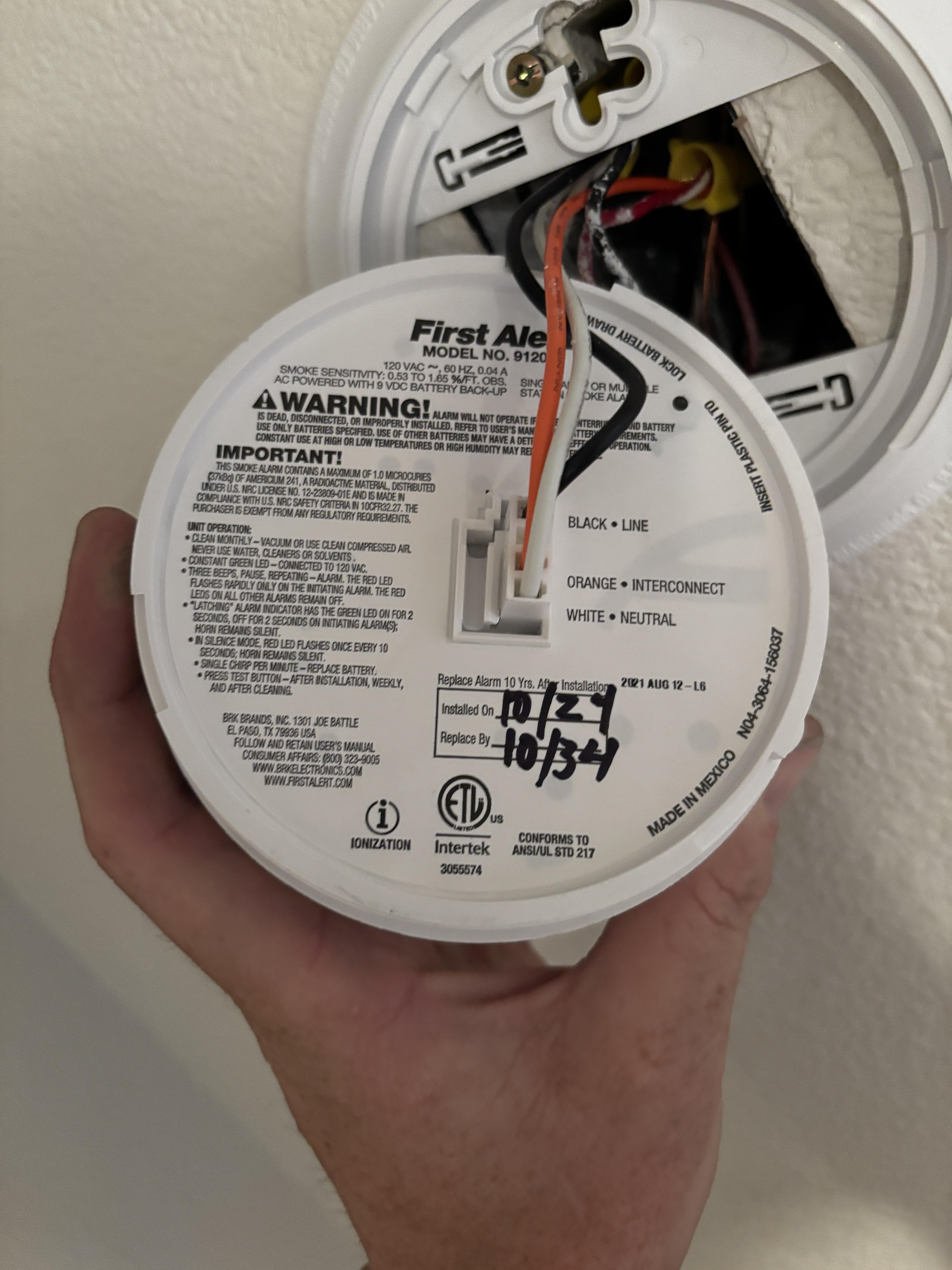 Hardwired smoke detector removed from its base showing wiring during replacement
