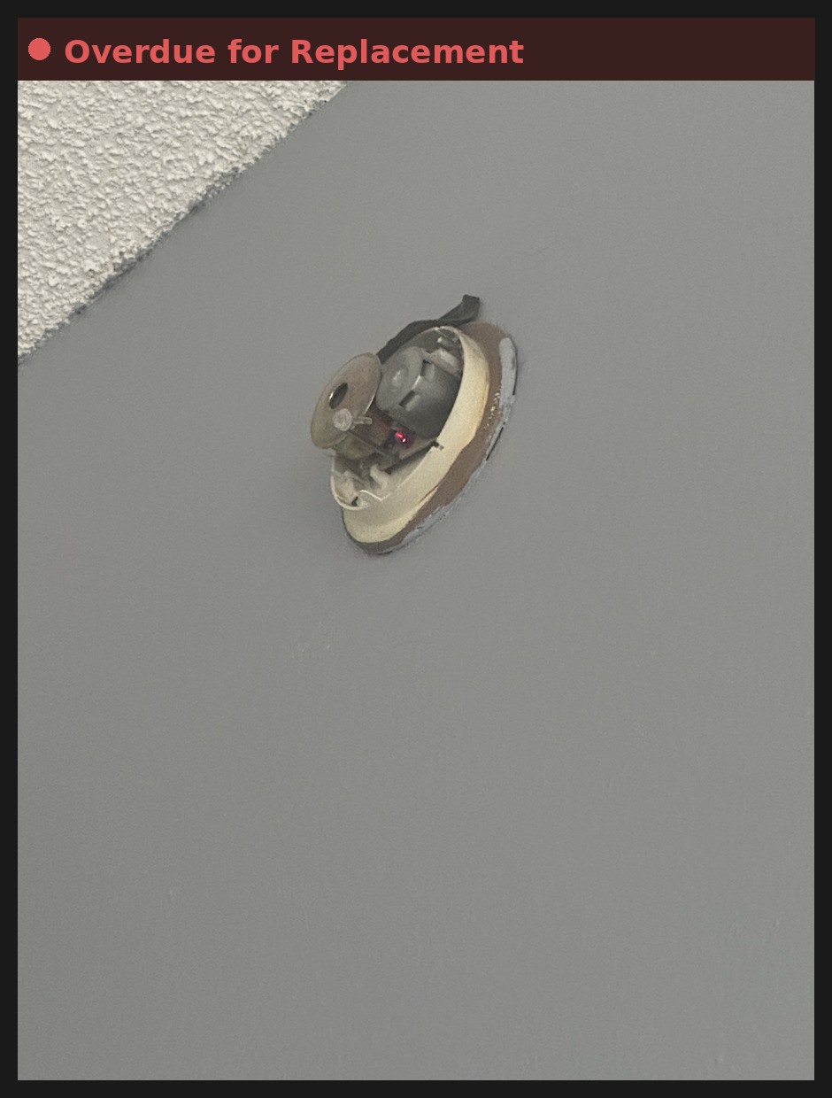 Old, yellowed smoke detector overdue for replacement on a ceiling