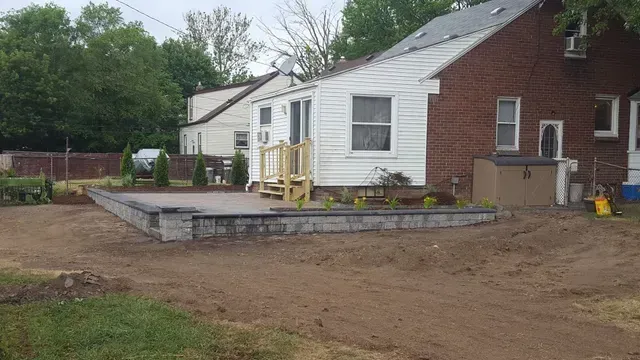 Finished residential backyard hardscape design showing a completed raised patio with gray block retaining walls, wood steps, and new softscaping.
