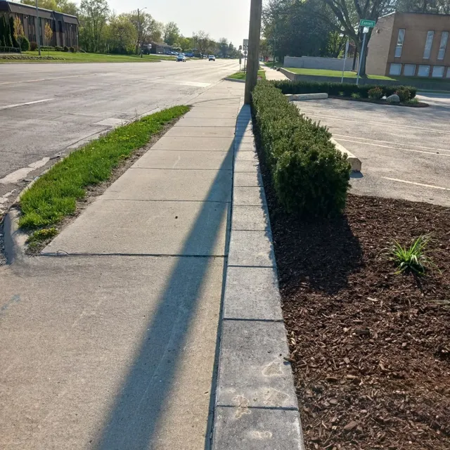 Commercial hardscape installation in Bloomfield Hills, showing a sidewalk, a low stone block border, and a new planter bed with shrubs and dark brown mulch.