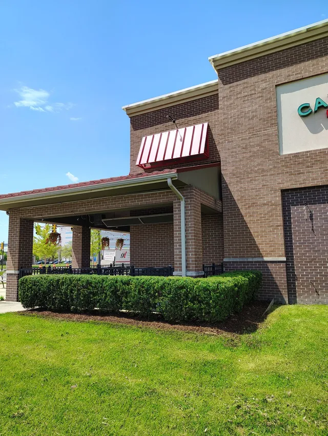 Well-maintained commercial lawn care at a business storefront in Troy, featuring a lush green lawn and neatly trimmed hedges in front of an outdoor patio area.