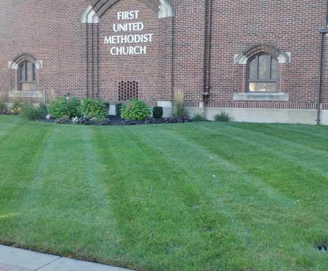 Expertly maintained commercial lawn care at a church, featuring a perfectly striped green lawn and trimmed landscaping in front of the brick building.