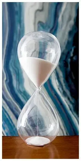 Clear glass hourglass with white sand on a wooden surface against a blue abstract background