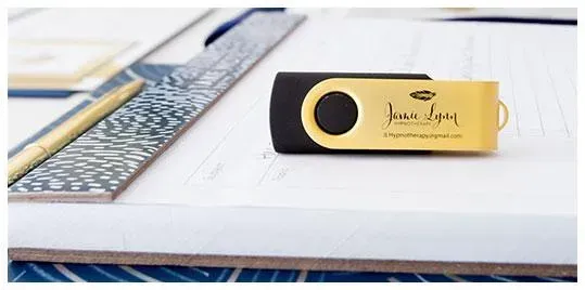 Gold and black USB flash drive on top of a clipboard with papers and a pen