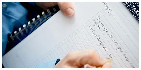 Close-up of a person writing affirmations in a notebook