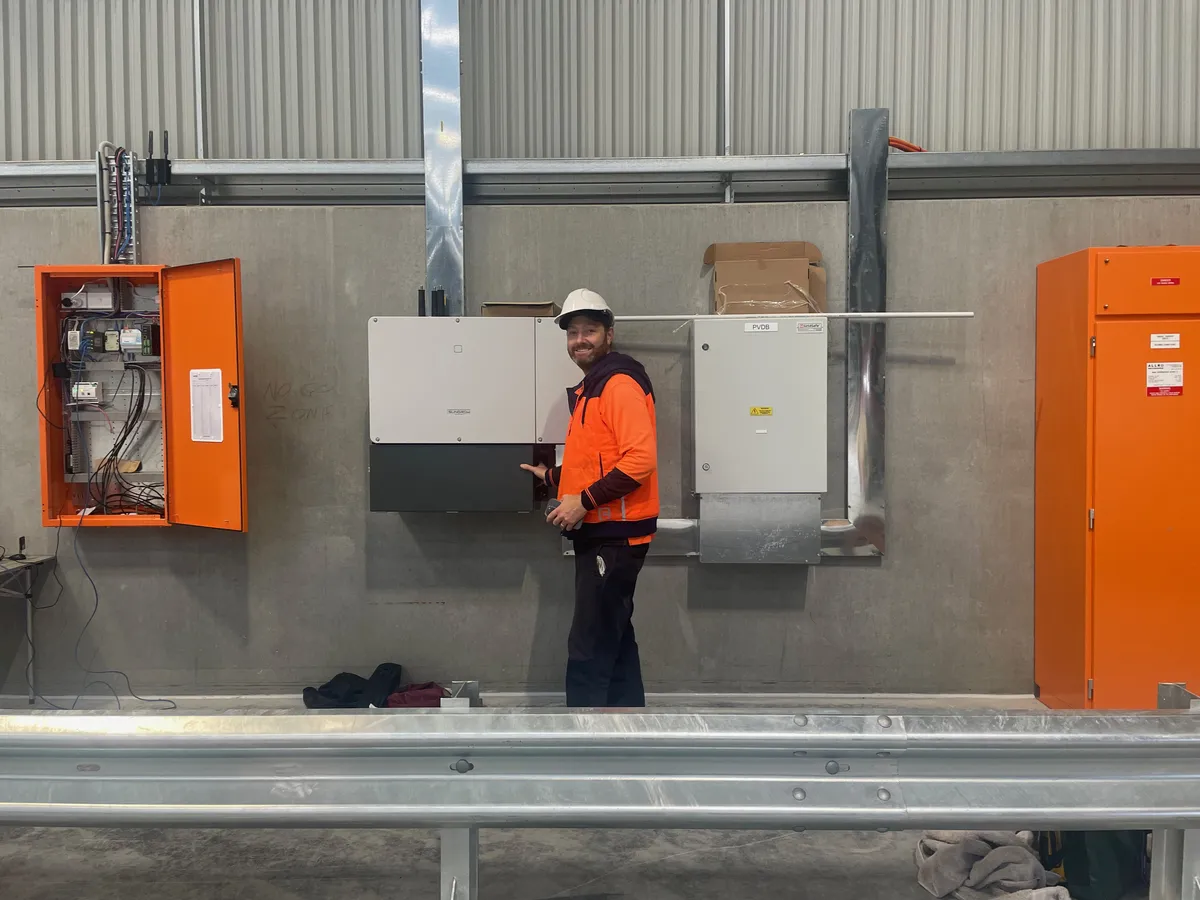 Pat Southwell at a commercial solar site with a large inverter and switchboard