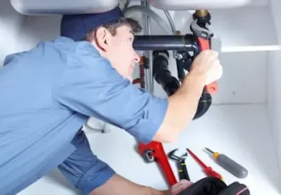 Licensed plumber repairing pipes beneath kitchen sink by Bexley Plumbing Pros