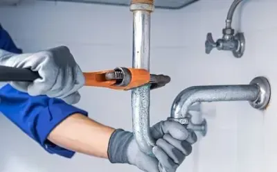 Plumber using pipe wrench on metal drain line beneath bathroom sink in Bexley