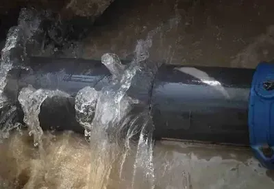 Water spraying from cracked underground pipe requiring emergency burst pipe repair