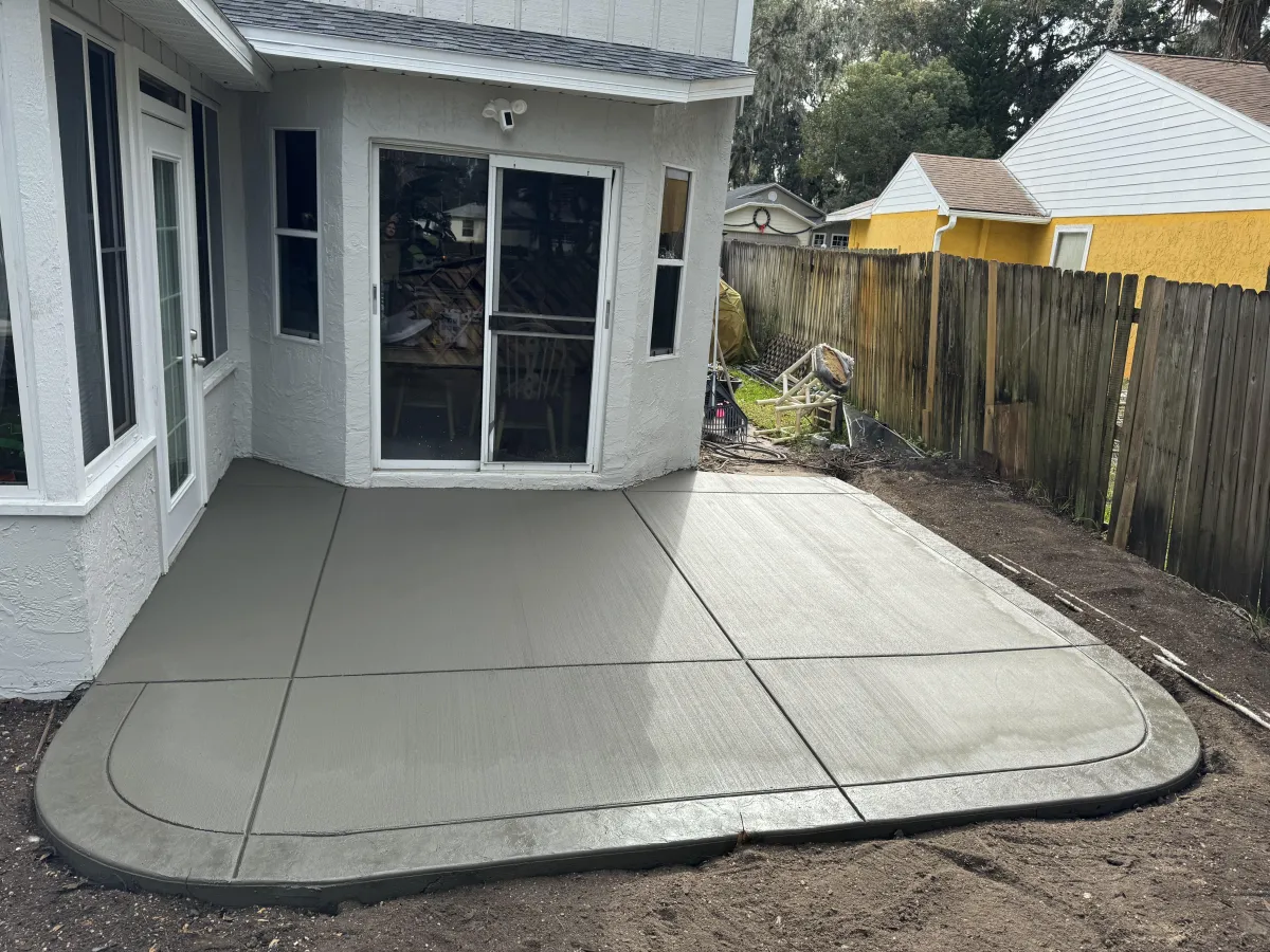 Residential concrete services icon featuring a house with a well-paved driveway, patio, and walkway in an orange color scheme. Ideal for driveways, patios, walkways, and home concrete projects.