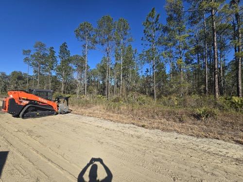 Kubota compact track loader on a freshly cleared lot with pine trees in Lake Helen, FL by J.F. Pro Services LLC.