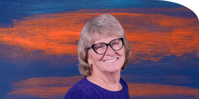Portrait of smiling therapist in front of a colorful sunset background, representing warmth and care.