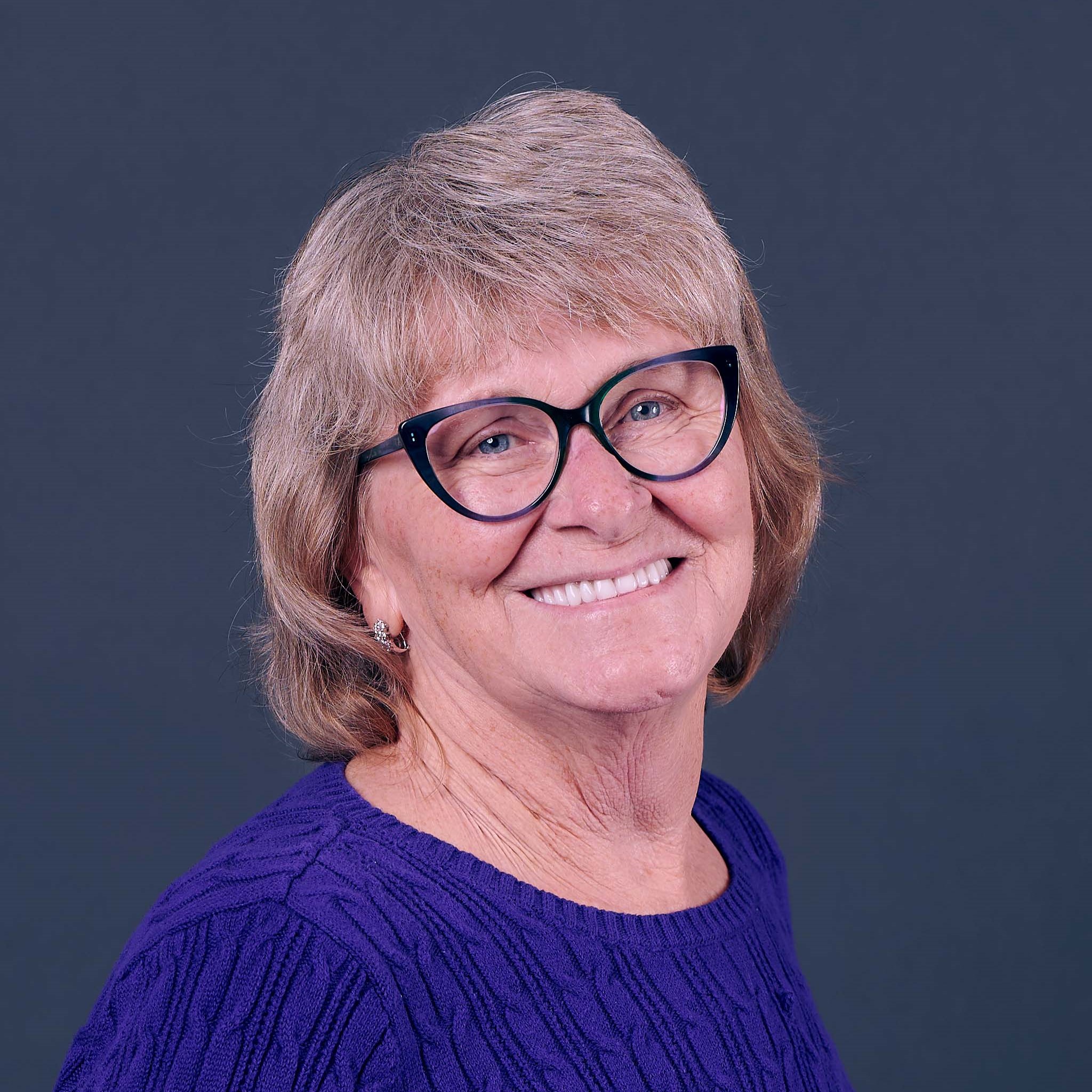 A professional therapist stands beside a wall displaying framed certificates and credentials, exuding confidence and trustworthiness. The therapist is dressed in business attire, with a gentle smile, and the background is a bright, organized office.