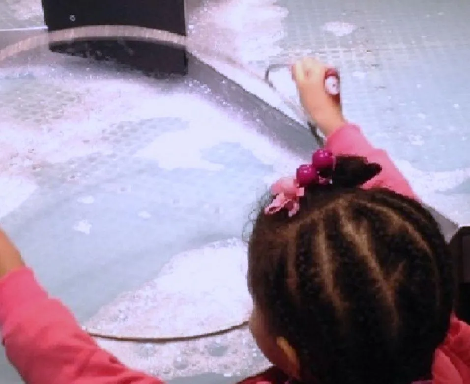 Child writes A in green sand