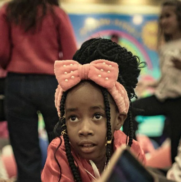 Brown skin girl holding a kazoo while watching the teacher on his laptop
