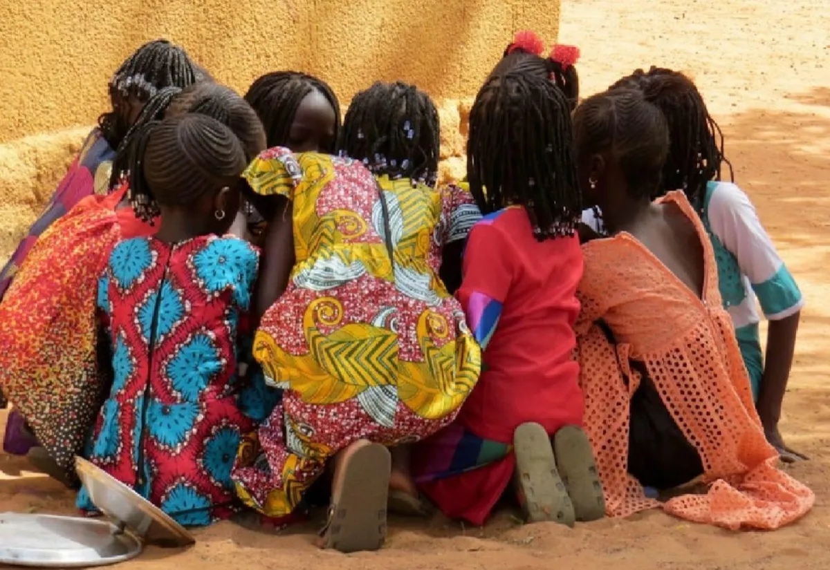 Students sit in a semicircle watching the teacher on a laptop