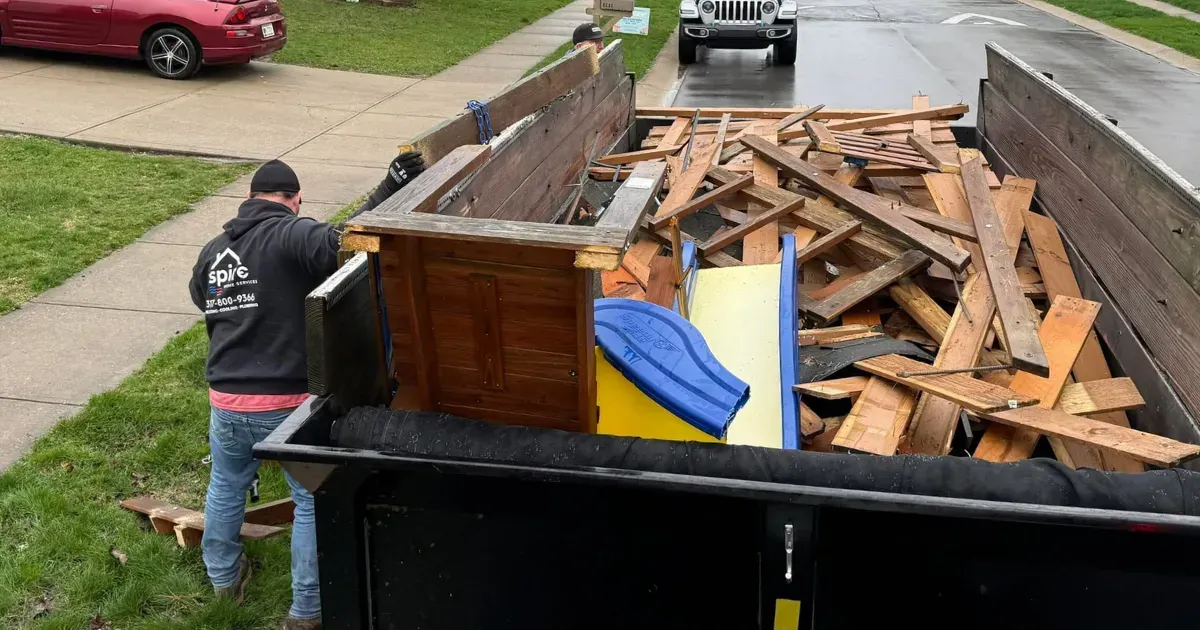 Worker loading a roll-off dumpster with wood debris from a demolished structure.