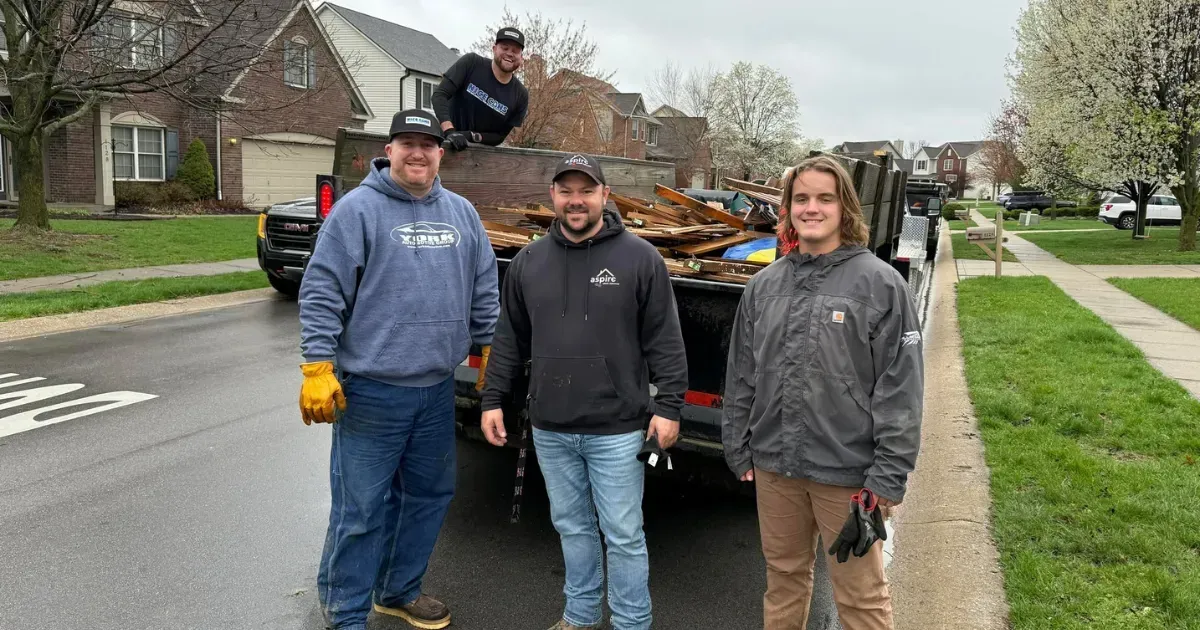Team of workers posing beside a full dumpster trailer loaded with wood waste.