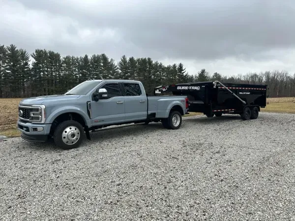  Sure-Trac roll-off dumpster loaded on a gooseneck trailer hitched to a heavy-duty truck.