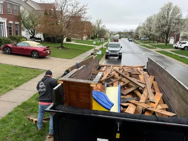  Man cleaning up a driveway full of wood debris and junk in a residential neighborhood.
