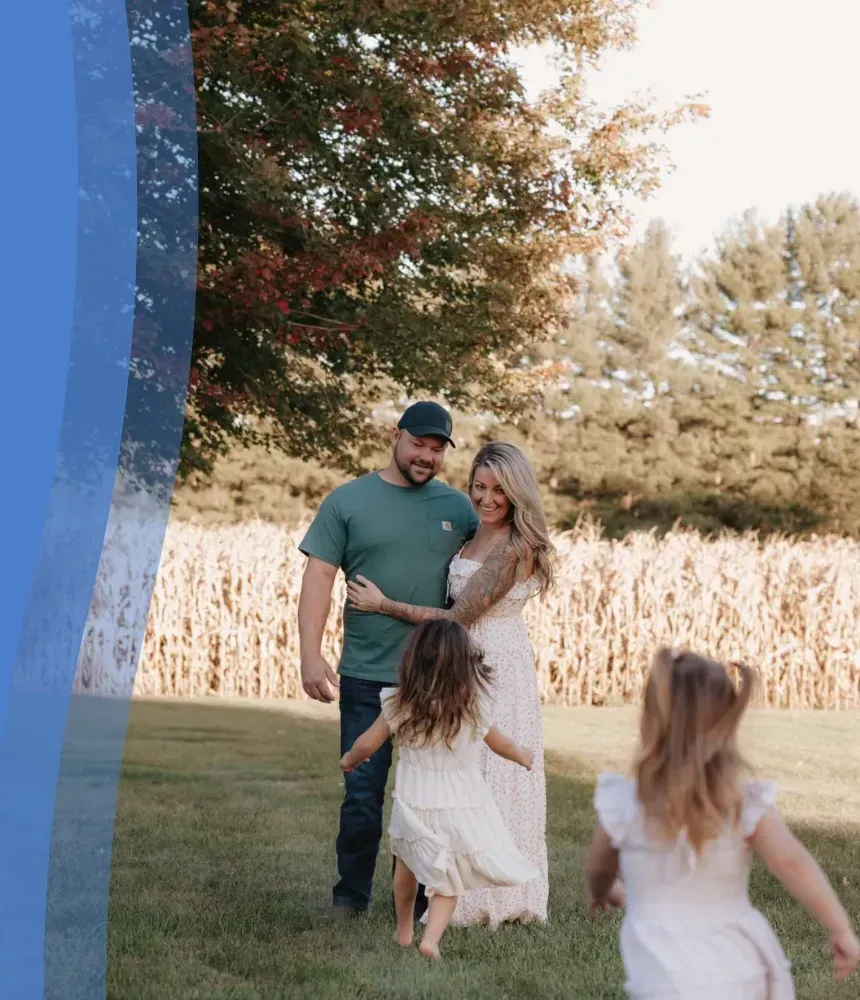 Family photo in a backyard near a cornfield with a blue wave overlay design on the left side.