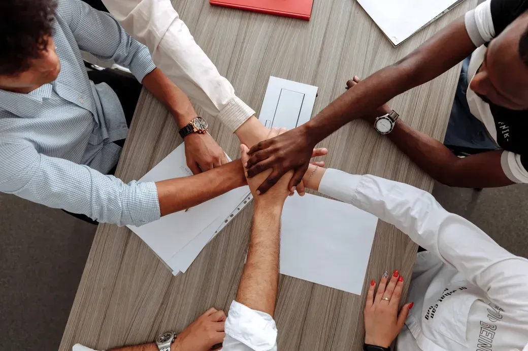 A group of business professionals joining hands in a collaborative gesture around a conference table