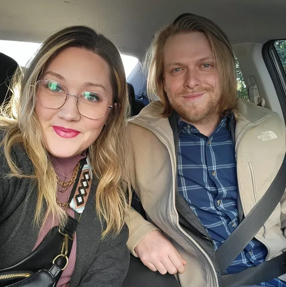 A man and woman sit together in the back seat of a car, appearing comfortable and engaged in discussion