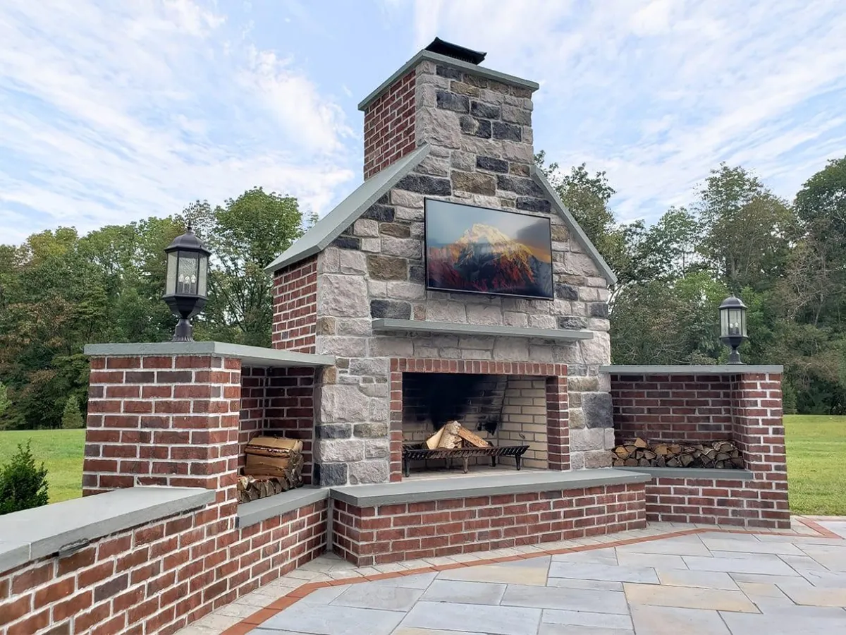 fields by duran: Luxury outdoor living space with brick and stone fireplace, mounted TV, and wood storage, set on a spacious patio.