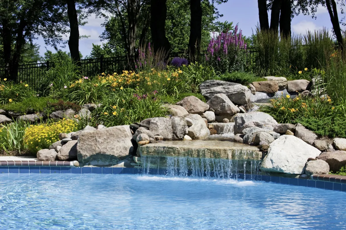 fields by duran: Backyard swimming pool with natural stone waterfall, surrounded by colorful flowers and lush landscaping.
