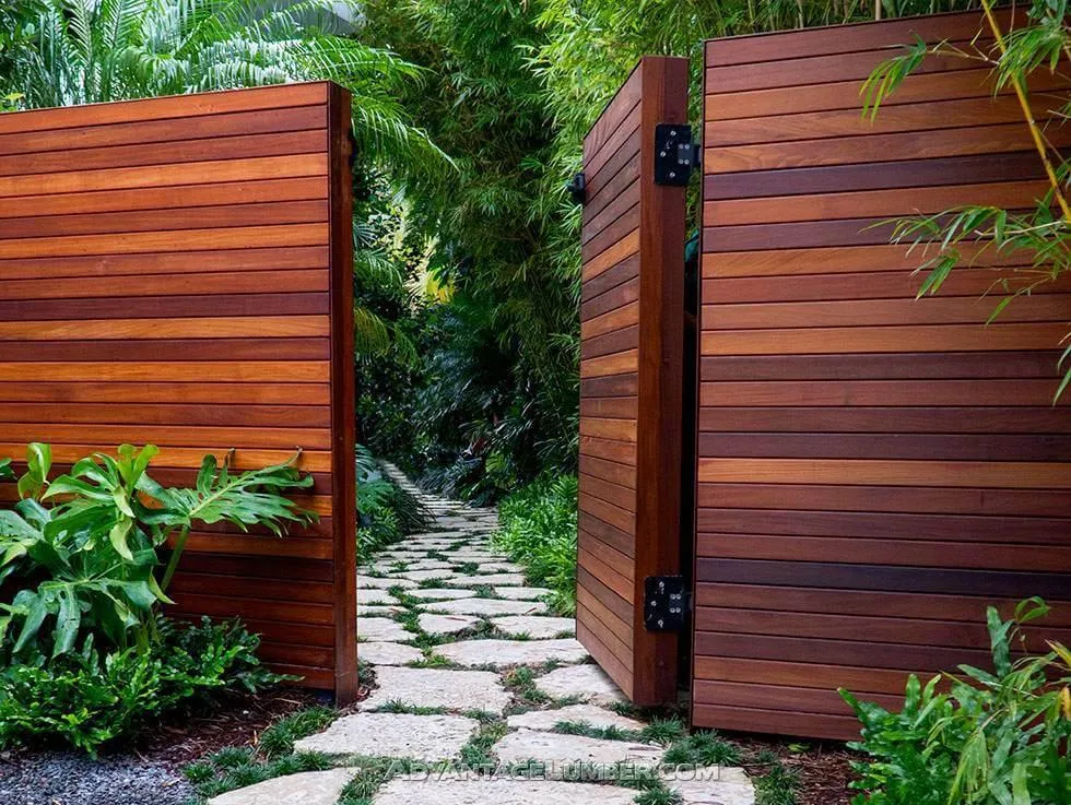 fields by duran: Modern wooden garden gate opening to a stone pathway surrounded by lush tropical plants.