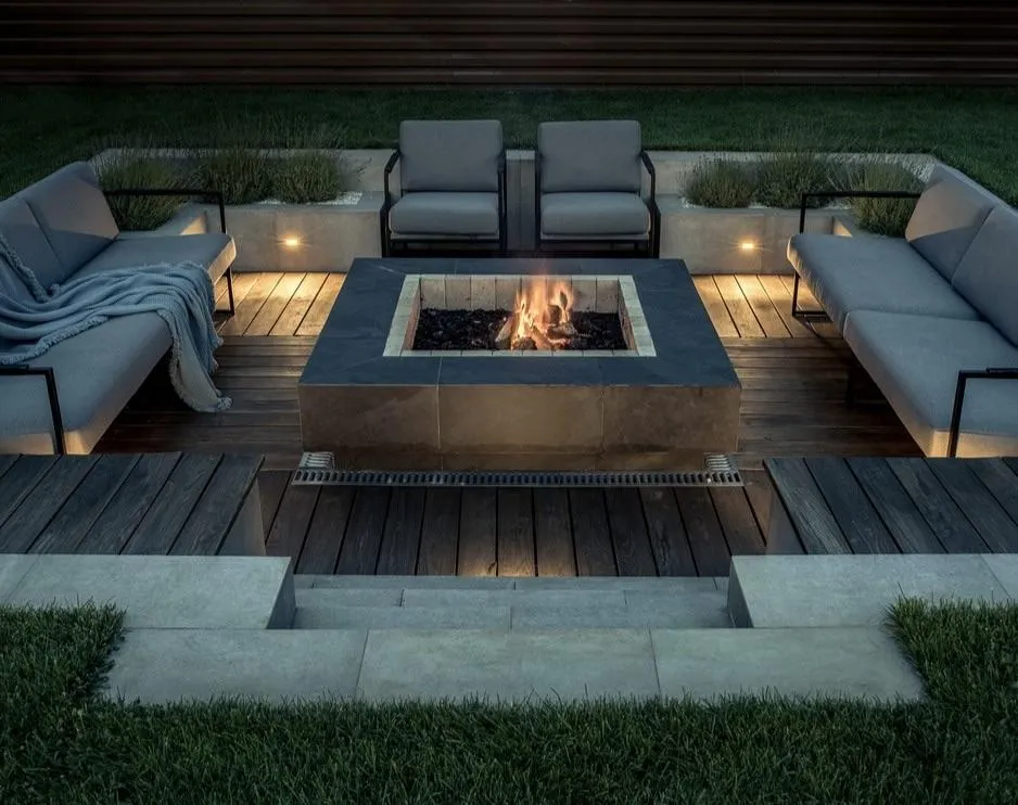 fields by duran: Modern outdoor patio with built-in fire pit, comfortable seating, wood decking, and ambient lighting for evening relaxation.