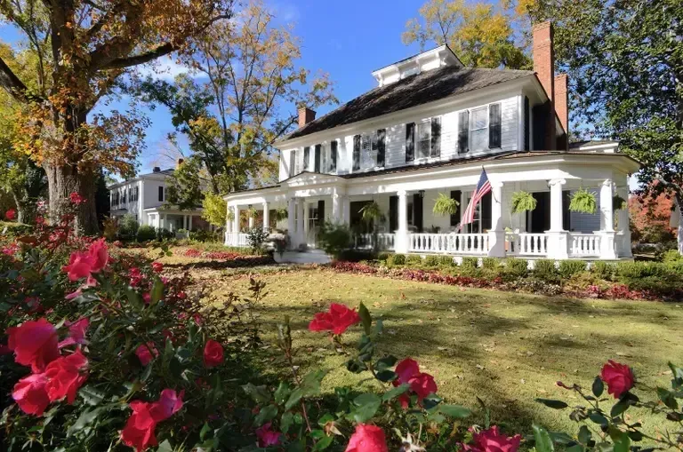fields by duran: Classic Southern-style home with large front porch, American flag, and landscaped garden with blooming flowers.