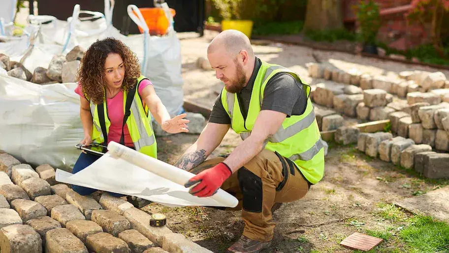 fields by duran: Landscape construction workers reviewing blueprints and installing stone pavers on a garden project.
