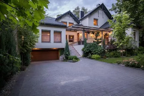 fields by duran: Contemporary home with a wide paver driveway, surrounded by mature trees and lush landscaping.