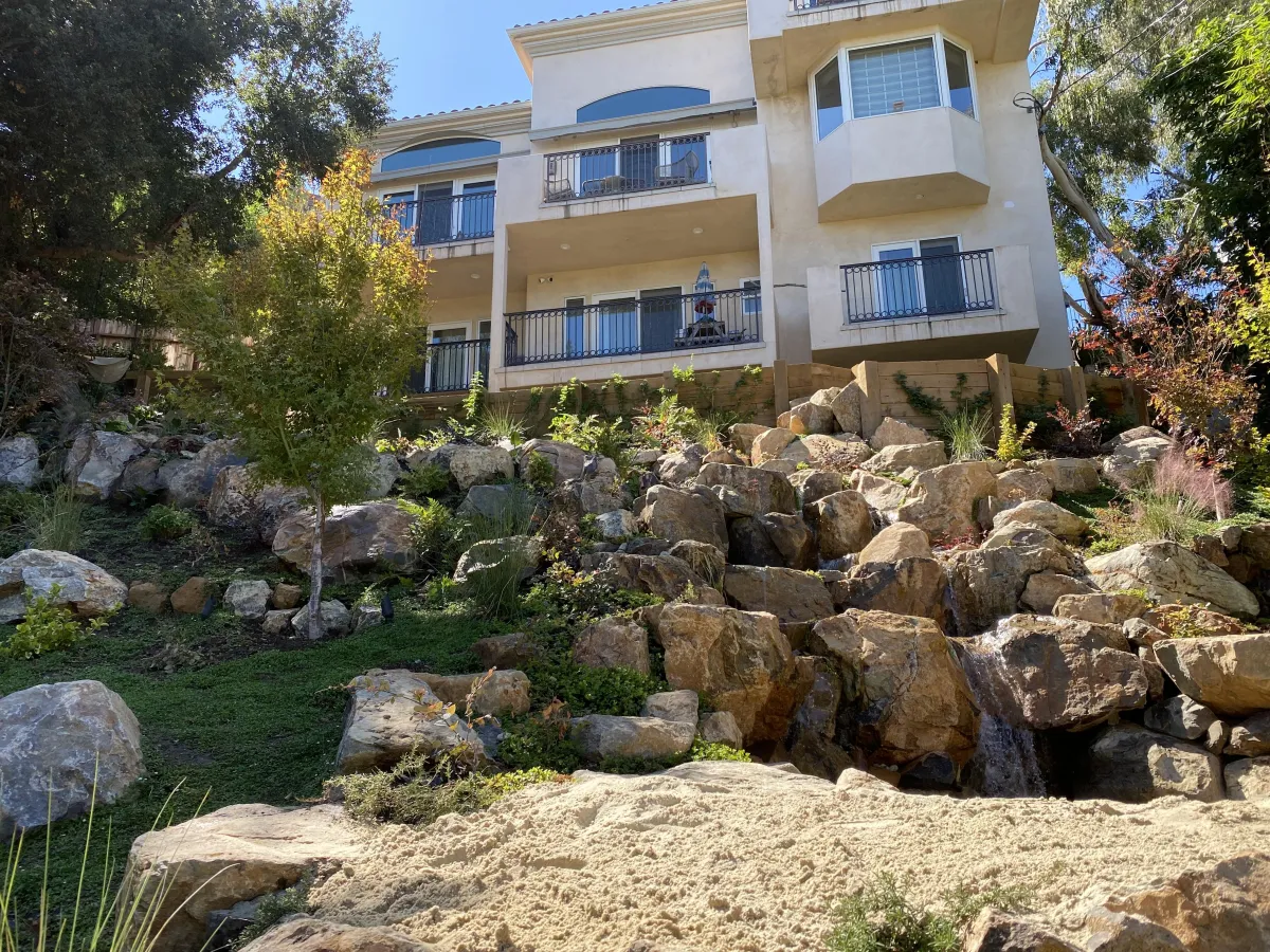 fields by duran: Beautiful landscaped backyard with stone fire pit, pond, waterfall, and mountain views at sunset.