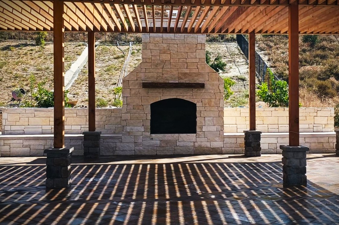 fields by duran: Luxury outdoor living space with brick and stone fireplace, mounted TV, and wood storage, set on a spacious patio.