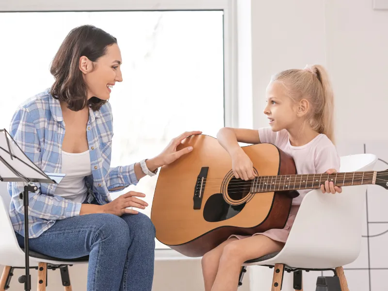 Two children playing an upright piano together, one focusing on the lower keys and the other on the higher ones. Both kids are smiling, engaged in playing, in a cozy room with warm lighting. The scene highlights the joy of collaborative music-making.