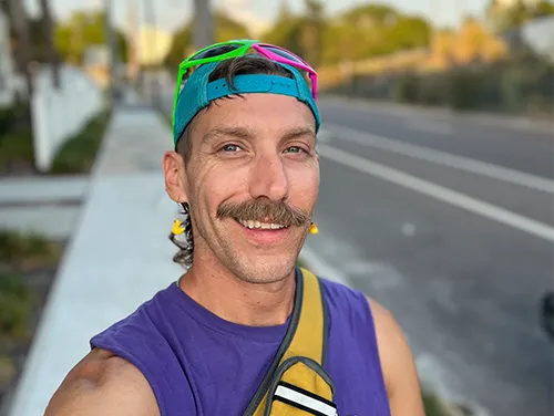 Adam Morrison walking in Saint Pete, Florida, with a green shirt and accessories, showcasing a relaxed, casual style.