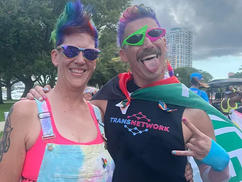 Adam and a friend proudly wearing rainbow attire at a local Pride event, celebrating inclusivity and self-expression with the TransNetwork community.