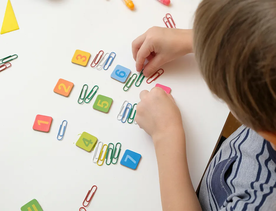 Child's hands arranging colorful paper clips and square manipulatives for math learning activity