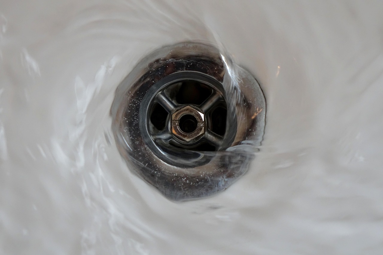 A close-up, top-down view of water swirling and flowing into an unclogged drain.