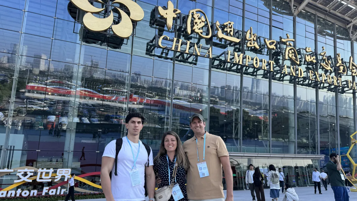 Femme souriante recevant un colis Canton Fair à la porte de son appartement moderne, lumière naturelle, ambiance chaleureuse