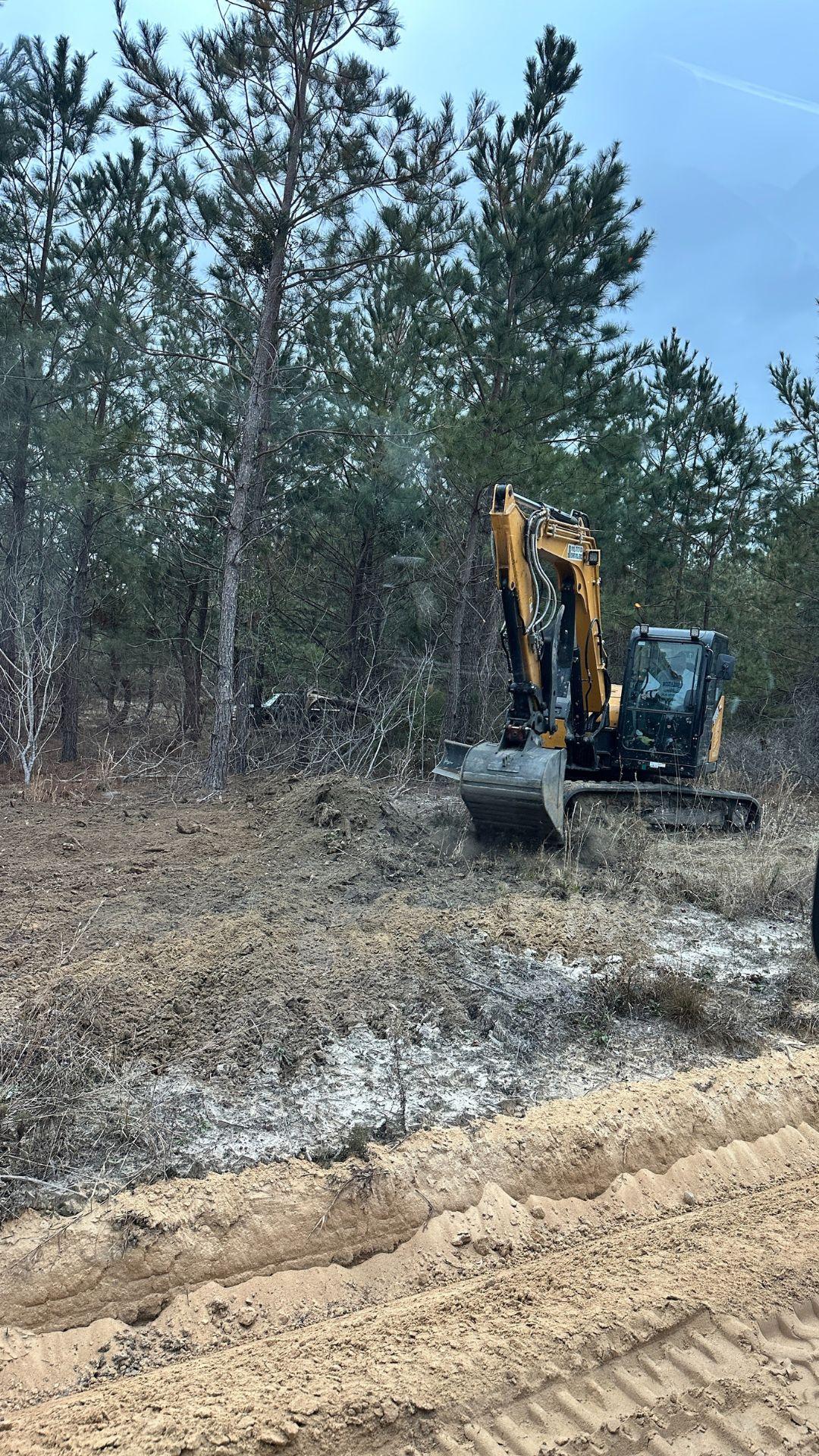 Excavator clearing brush and small trees on a rural property surrounded by pine trees during a land clearing project by Vaquero Landworks in Middle Georgia.