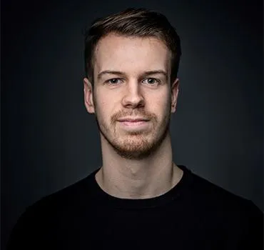A diverse team of three business coaches, two women and one man, standing together in a sunlit workspace. They are dressed professionally, smiling, and holding notebooks. 1:1 aspect ratio.