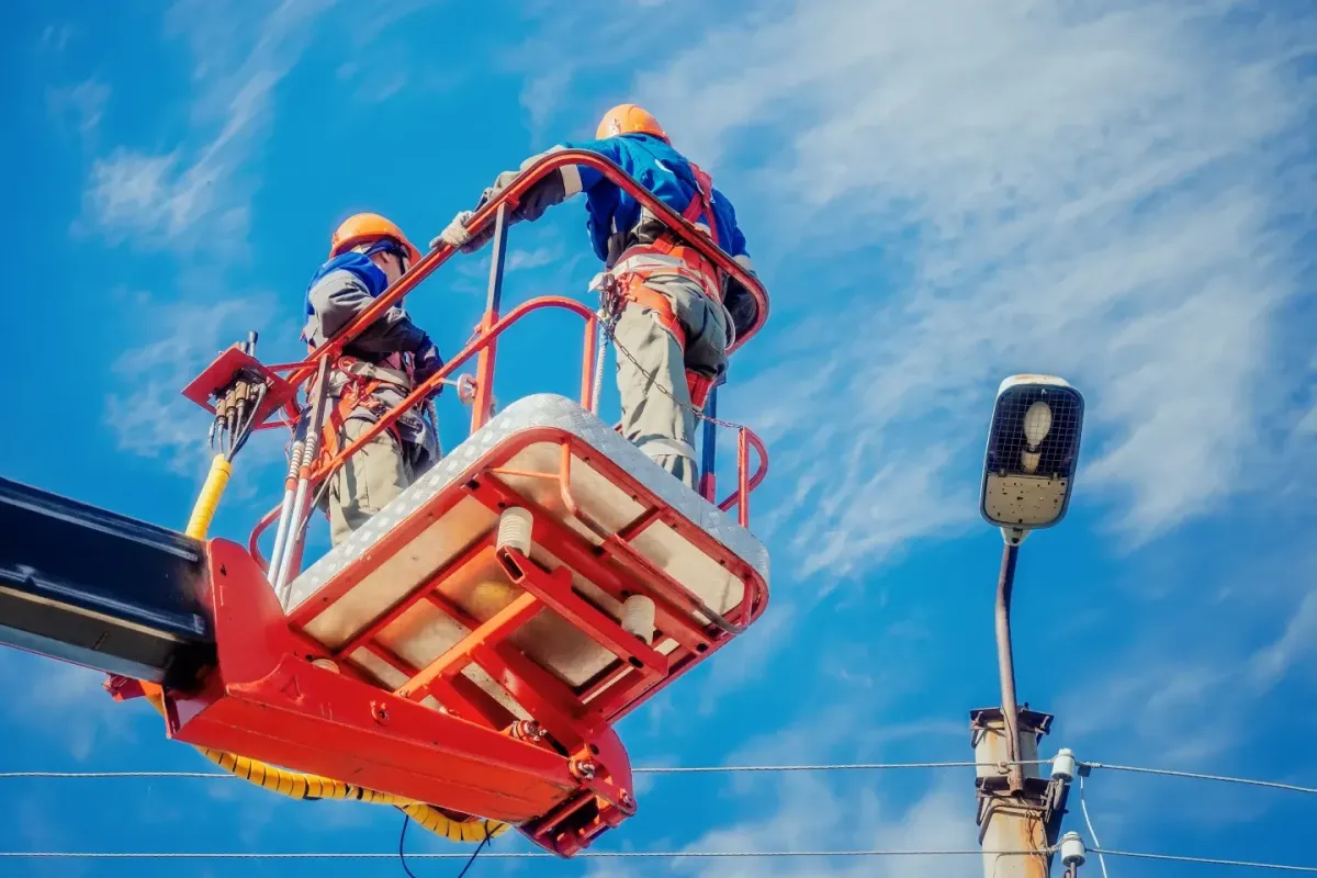 Two workers in safety gear operating an elevated work platform near power lines, representing safety training and worksite compliance