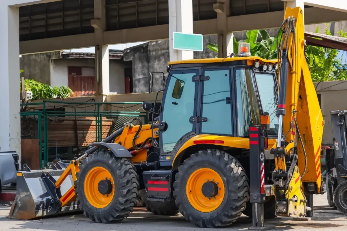 Yellow backhoe loader parked at a construction site with front bucket and rear excavator arm visible