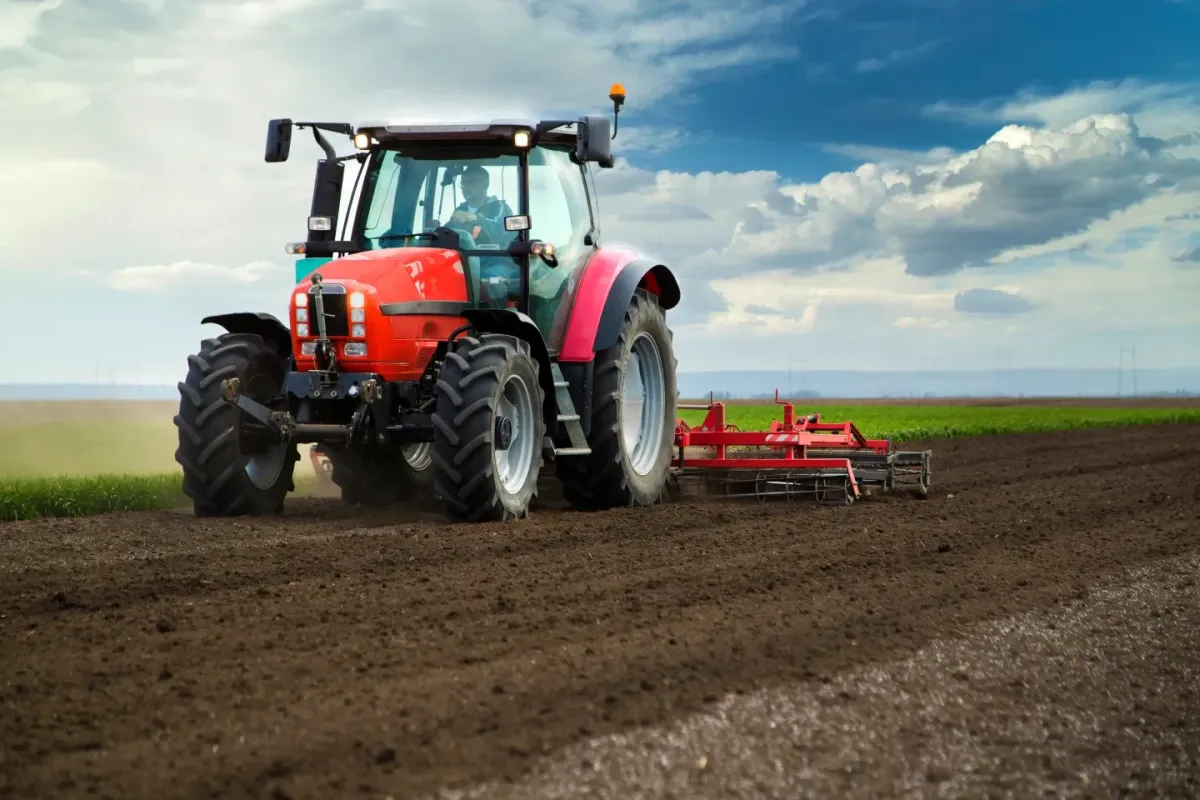 Red tractor preparing farmland in an open agricultural field under a cloudy sky