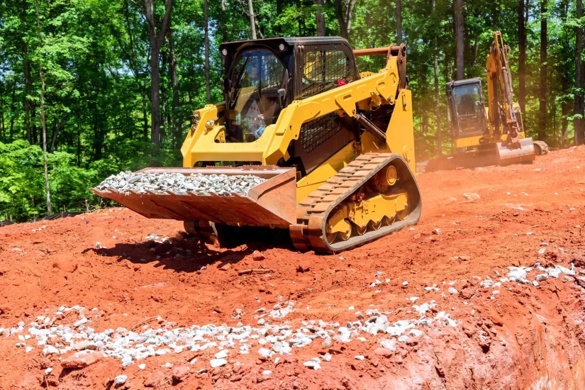 Tracked skid steer loader moving over red soil at an earthmoving and construction site