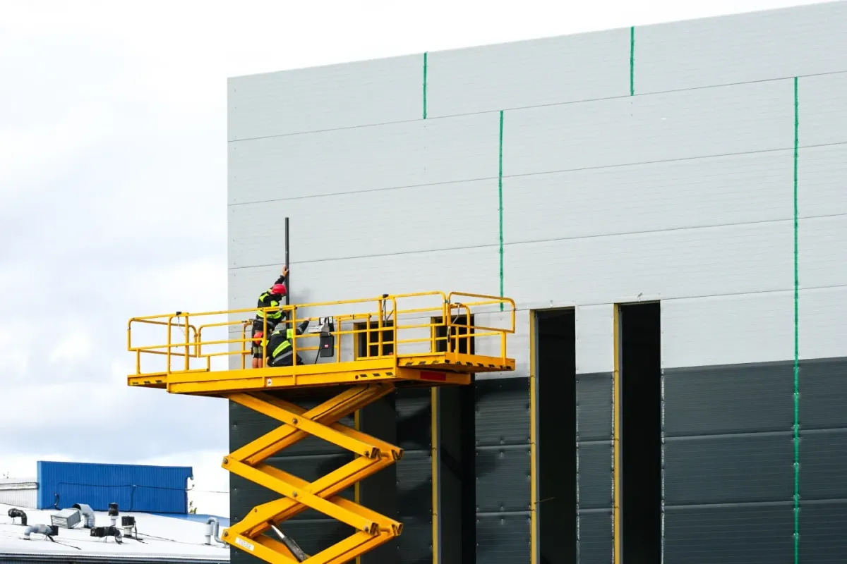 Worker operating a yellow scissor lift beside a commercial building during elevated work platform operations