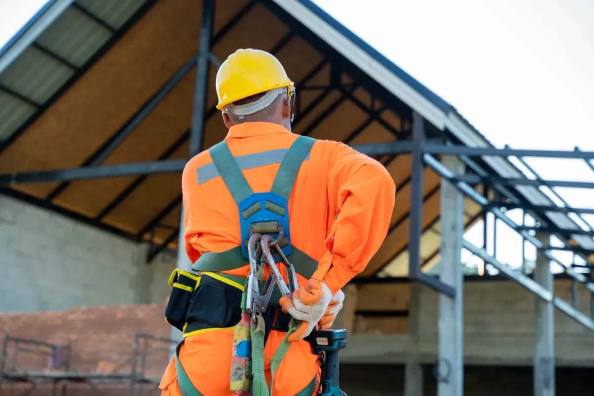 Construction worker in high-visibility clothing and fall protection equipment standing at a building frame